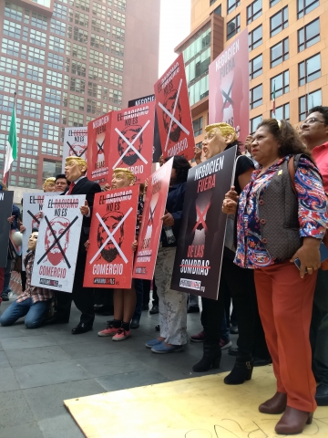 A group of people, some of them wearing Donald Trump masks, standing with protest banners